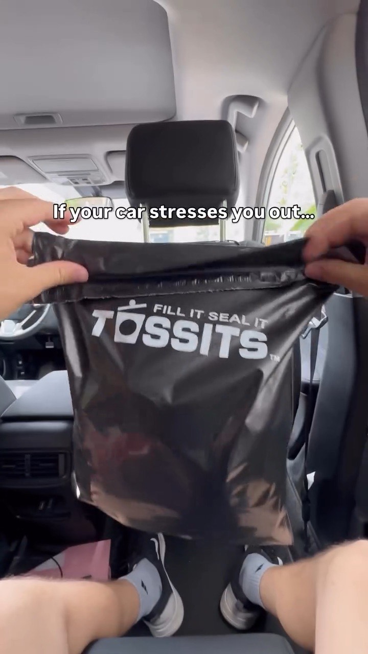 Hands hold up a black Tossits bag hung from a car seat