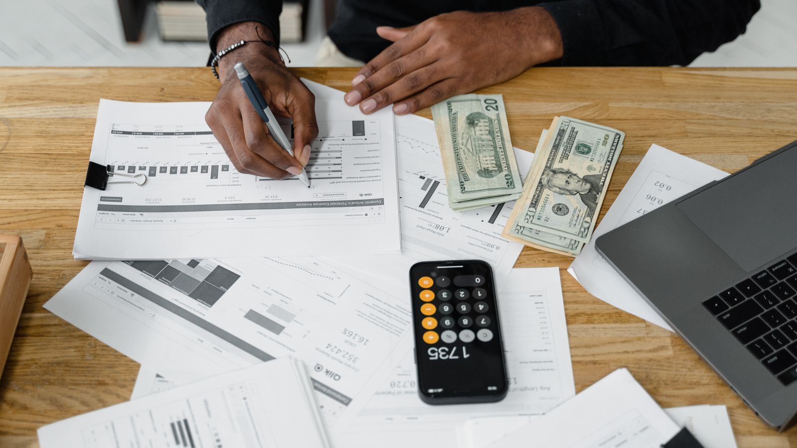 An accountant's desk with financial reports, a calculator, cash, and a laptop