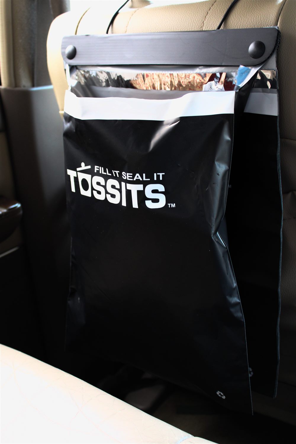 A black Tossits fill it seal it car trash bag hanging from a car headrest